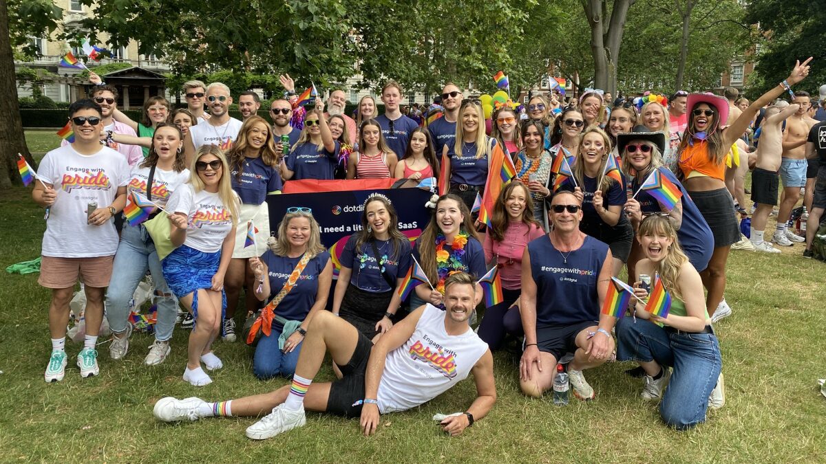 Photo of around 40 Dotdigital employees in a park smiling at the camera, celebrating Pride, wearing Pride t shirts with rainbow colors