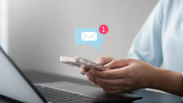 A marketer holds a smartphone with an email notification bubble showing a new email icon.
