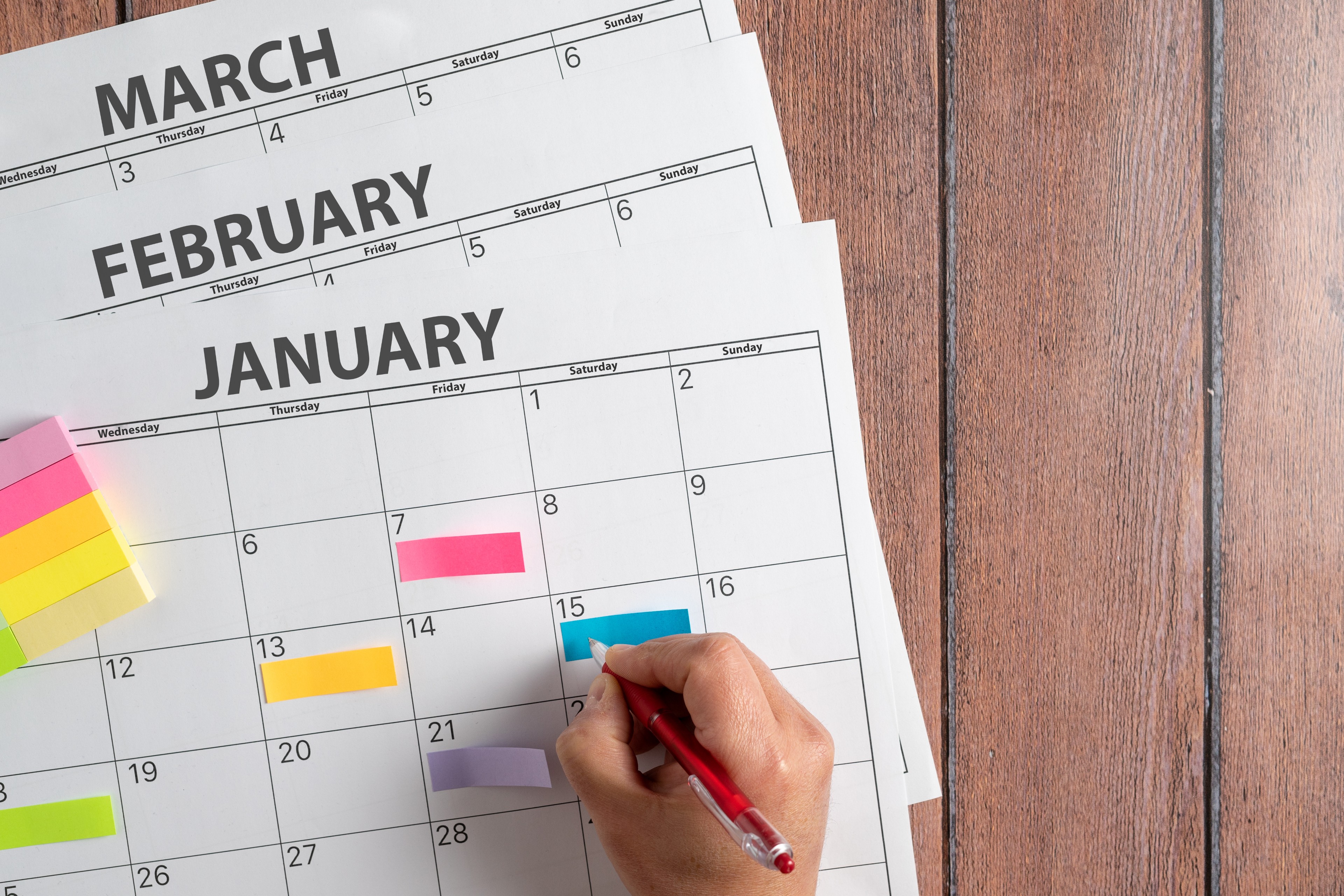 View from above of a person's hand making notes on a calendar with the first months of the year 