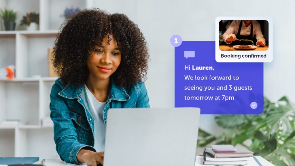 A smiling young woman with curly hair looks at a laptop screen, receiving an automated message.